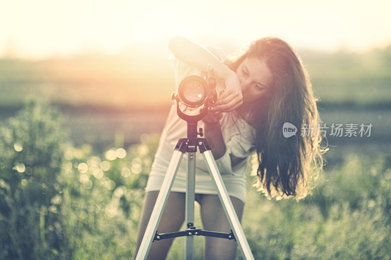 Woman setting up telescope in the field at sunset